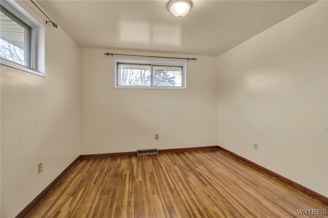 empty room with wood finished floors, visible vents, and baseboards