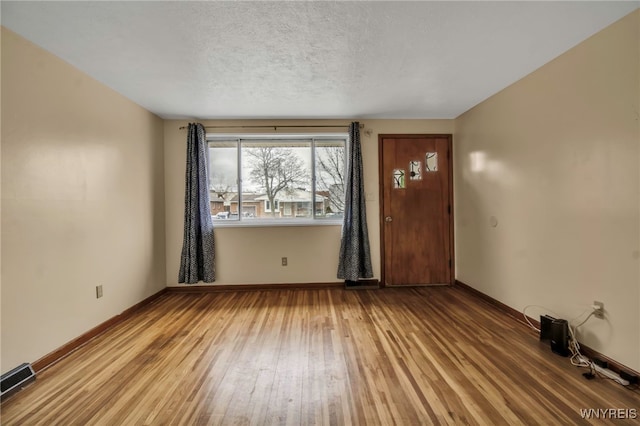 unfurnished room with a textured ceiling, light wood finished floors, visible vents, and baseboards