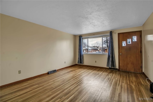 interior space with baseboards, a textured ceiling, visible vents, and wood finished floors