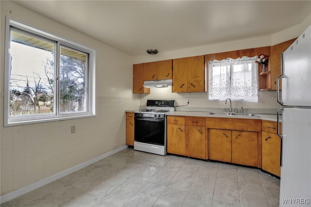 kitchen featuring under cabinet range hood, white appliances, a sink, light countertops, and brown cabinets