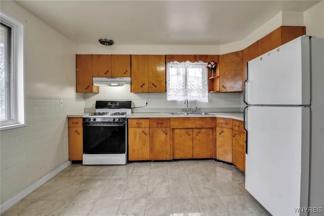 kitchen featuring under cabinet range hood, a sink, range with gas stovetop, light countertops, and freestanding refrigerator