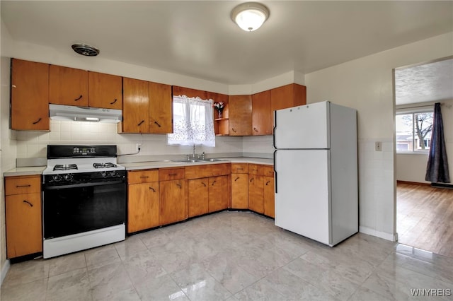 kitchen featuring under cabinet range hood, a sink, light countertops, freestanding refrigerator, and range with gas cooktop