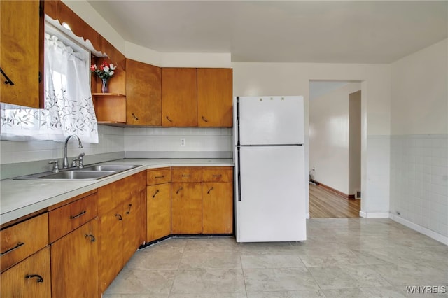 kitchen with a sink, light countertops, freestanding refrigerator, open shelves, and brown cabinetry