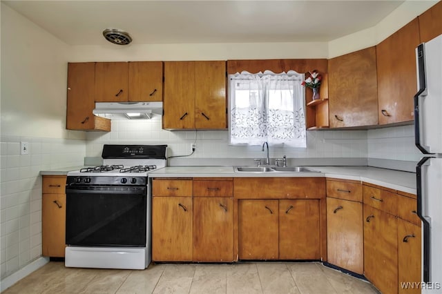 kitchen with gas range oven, light countertops, freestanding refrigerator, a sink, and under cabinet range hood