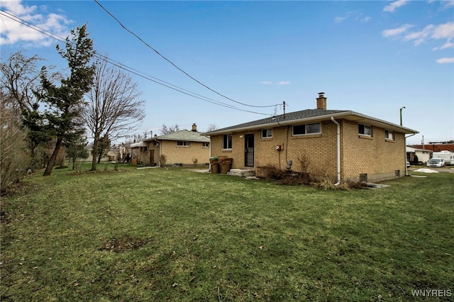 rear view of property with brick siding, a lawn, and a chimney