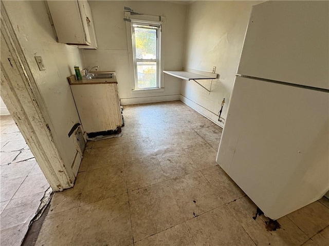 kitchen with white cabinetry, a sink, and freestanding refrigerator