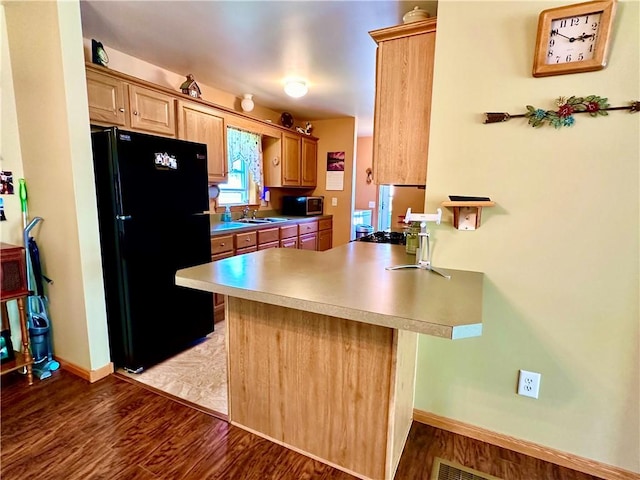 kitchen with a peninsula, a sink, wood finished floors, freestanding refrigerator, and stainless steel microwave