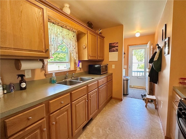 kitchen featuring baseboards, stainless steel microwave, brown cabinets, light countertops, and a sink