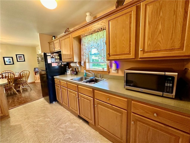 kitchen with light countertops, freestanding refrigerator, stainless steel microwave, and a sink