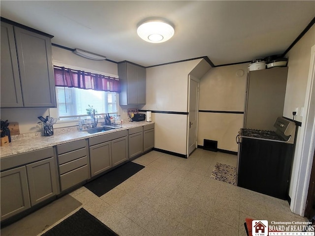 kitchen with gas range oven, gray cabinets, light countertops, light floors, and a sink