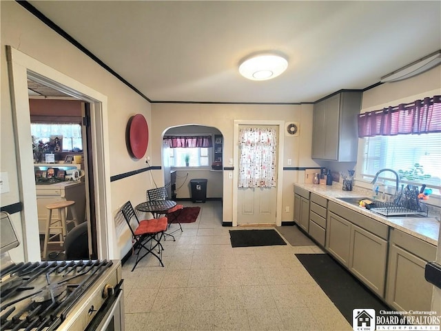 kitchen featuring arched walkways, light countertops, gray cabinetry, light floors, and a sink