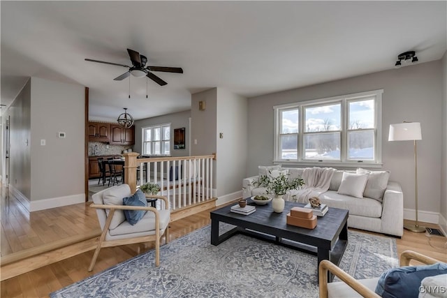 living room with visible vents, light wood-type flooring, a ceiling fan, and baseboards