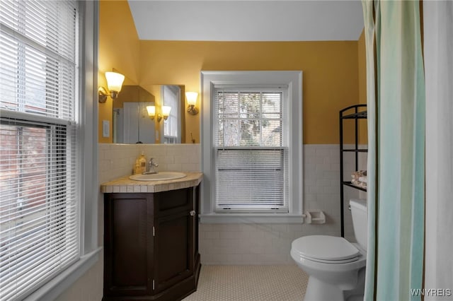 bathroom with wainscoting, toilet, tile patterned floors, vanity, and tile walls