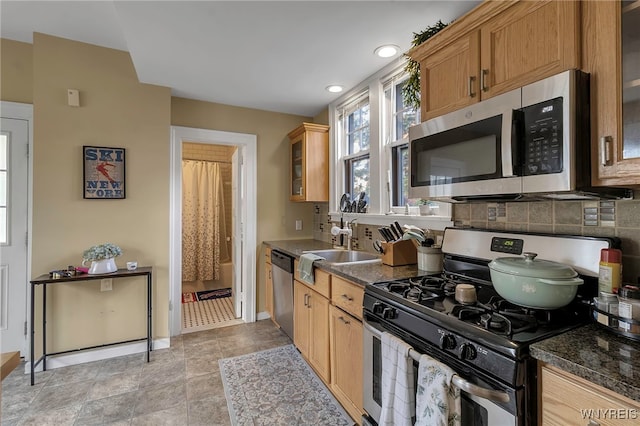 kitchen with dark countertops, glass insert cabinets, a sink, stainless steel appliances, and backsplash