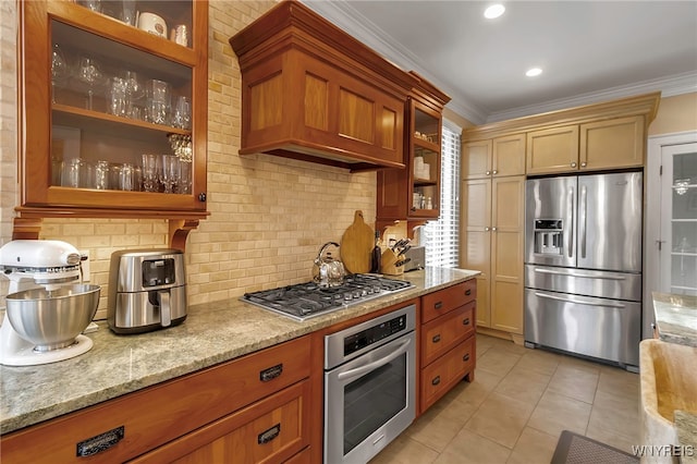 kitchen with light tile patterned floors, light stone counters, stainless steel appliances, backsplash, and crown molding