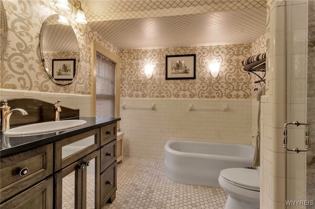 full bathroom with tile patterned flooring, toilet, tile walls, wainscoting, and wallpapered walls