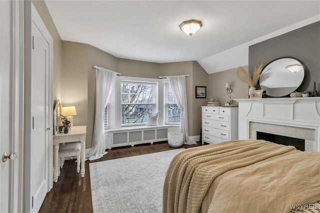 bedroom with baseboards, radiator heating unit, dark wood-style flooring, vaulted ceiling, and a fireplace