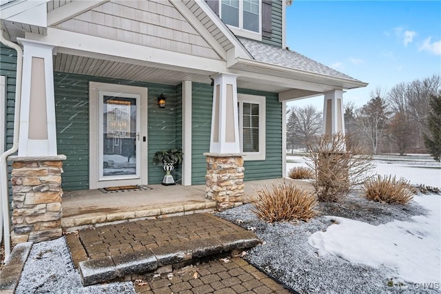 snow covered property entrance featuring a porch and a shingled roof