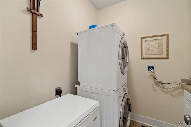 clothes washing area featuring baseboards, stacked washer / dryer, cabinet space, and tile patterned floors