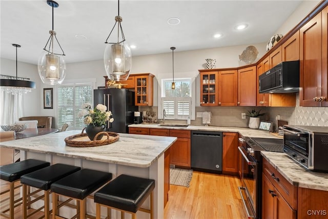 kitchen featuring light wood finished floors, a toaster, brown cabinets, a kitchen breakfast bar, and black appliances