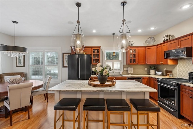 kitchen with decorative backsplash, appliances with stainless steel finishes, light wood-style floors, glass insert cabinets, and a kitchen breakfast bar