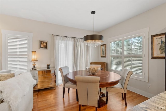 dining room with baseboards, light wood finished floors, and a notable chandelier