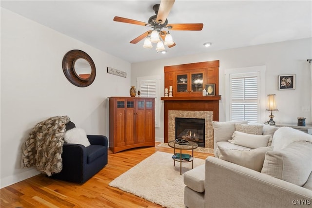 living area featuring light wood-style floors, a glass covered fireplace, and a ceiling fan