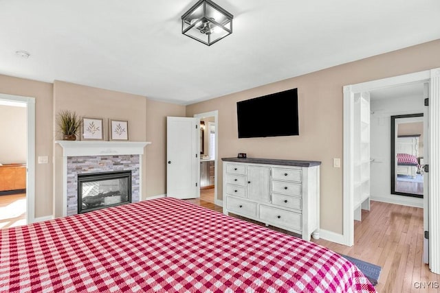 bedroom with light wood-type flooring, a stone fireplace, and baseboards