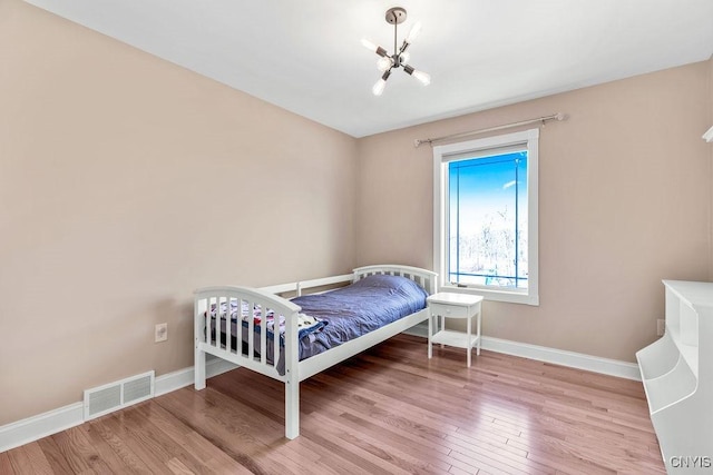 bedroom with an inviting chandelier, wood finished floors, visible vents, and baseboards