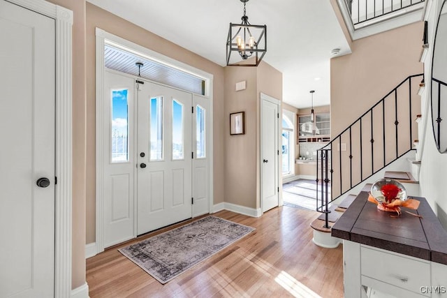 foyer with an inviting chandelier, a healthy amount of sunlight, light wood finished floors, and stairs