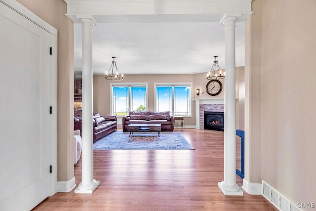 living area featuring ornate columns, a notable chandelier, wood finished floors, and a lit fireplace