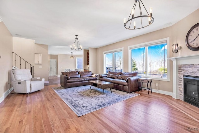 living room with a chandelier, a stone fireplace, wood finished floors, and baseboards