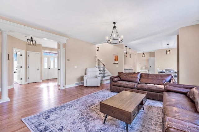 living area featuring a chandelier, stairway, wood finished floors, and decorative columns