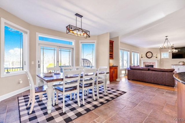 dining area featuring stone tile floors, a fireplace, baseboards, and a chandelier