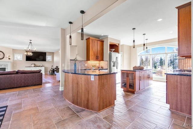 kitchen with decorative backsplash, stainless steel fridge with ice dispenser, brown cabinets, stone tile flooring, and a fireplace