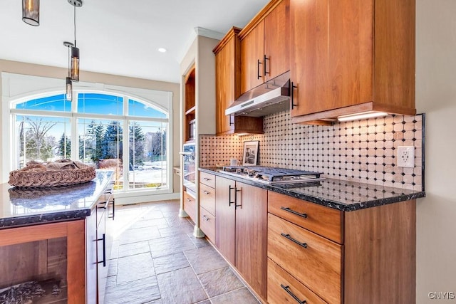 kitchen with stone tile floors, brown cabinetry, stainless steel appliances, under cabinet range hood, and backsplash