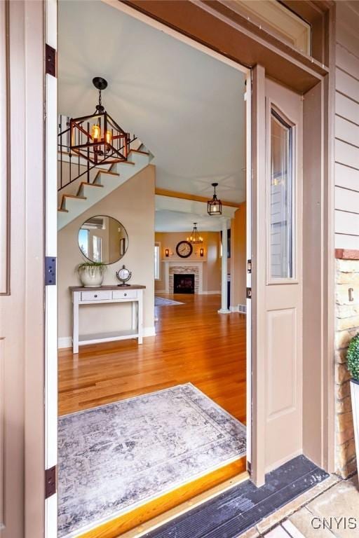 foyer featuring baseboards, a fireplace with flush hearth, stairway, and wood finished floors