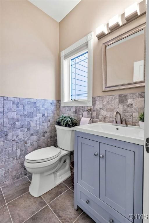 bathroom with tile patterned flooring, toilet, a wainscoted wall, vanity, and tile walls