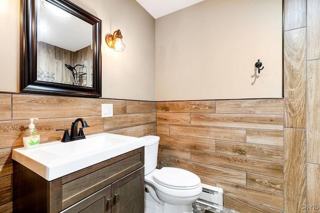 half bath with toilet, a wainscoted wall, vanity, tile walls, and baseboard heating