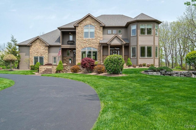 view of front of property featuring a shingled roof, stone siding, and a front lawn