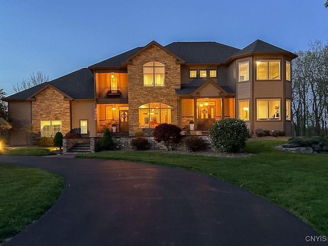 view of front of house with a balcony, stone siding, and a front yard