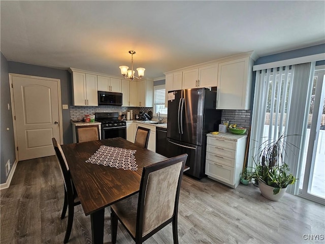 kitchen featuring a notable chandelier, wood finished floors, light countertops, black range with gas stovetop, and freestanding refrigerator