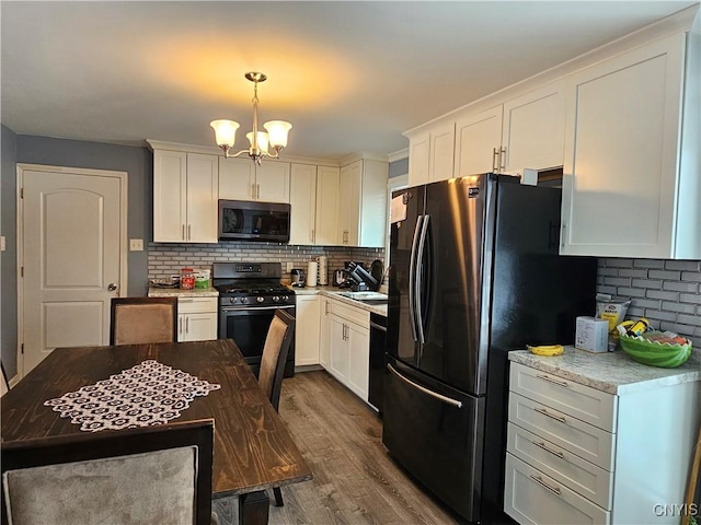 kitchen with a chandelier, wood finished floors, a sink, decorative backsplash, and black appliances