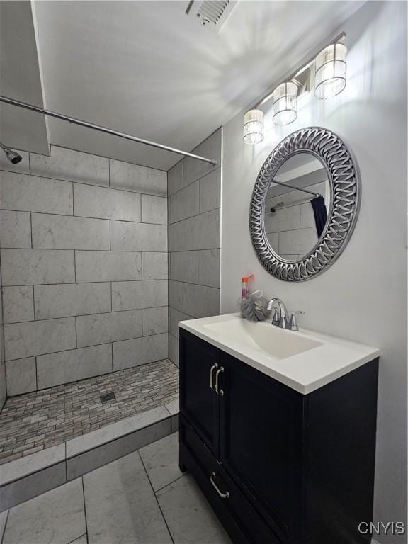 bathroom featuring tiled shower, vanity, and visible vents