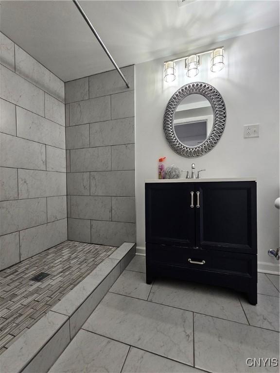 bathroom with a tile shower, vanity, and baseboards