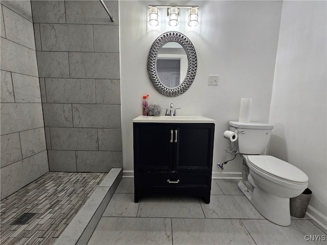 full bathroom featuring baseboards, a tile shower, vanity, and toilet