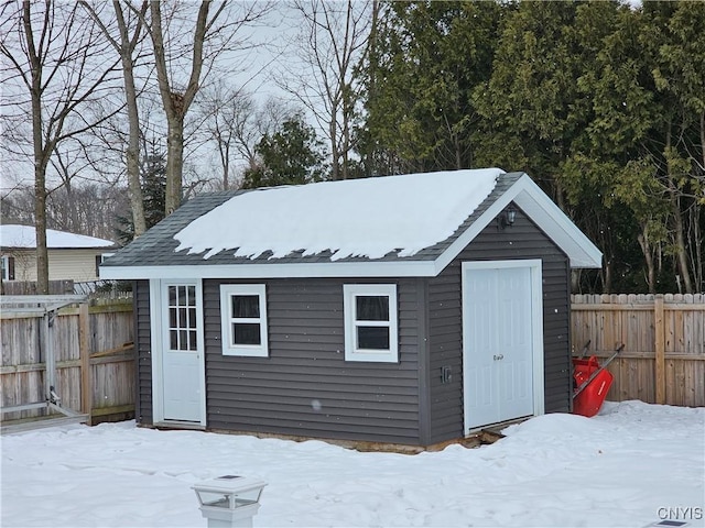 snow covered structure with a fenced backyard and an outdoor structure