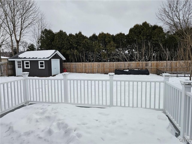 snow covered patio with an outbuilding, a fenced backyard, and a shed