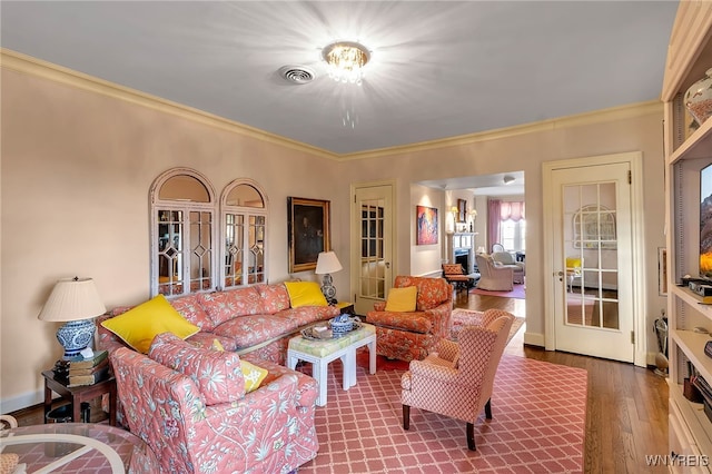 living area featuring wood finished floors, visible vents, baseboards, french doors, and crown molding