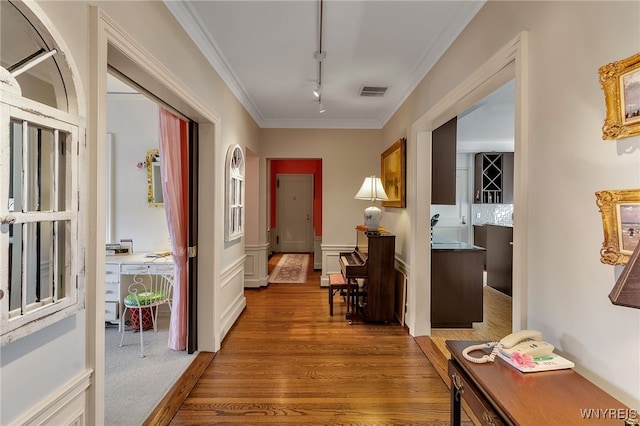 hallway with rail lighting, visible vents, crown molding, and wood finished floors